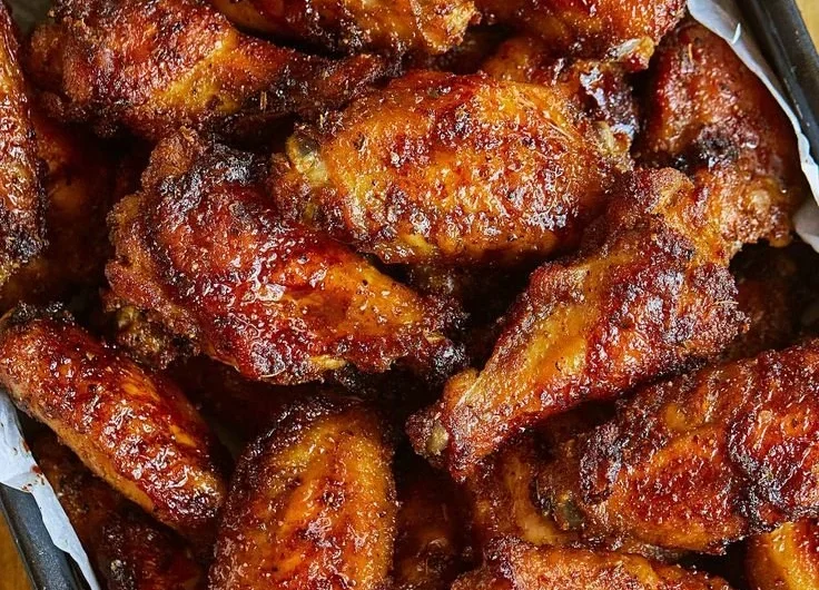 Plate of juicy chicken wings garnished with herbs and served with dipping sauce