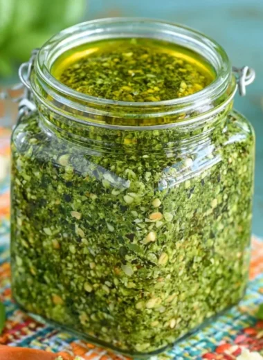 Fresh basil pesto in a glass jar with ingredients nearby