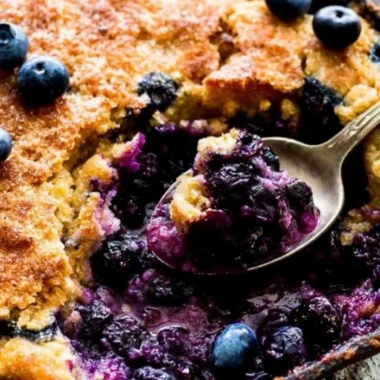 Homemade blueberry cobbler topped with golden crust and fresh berries