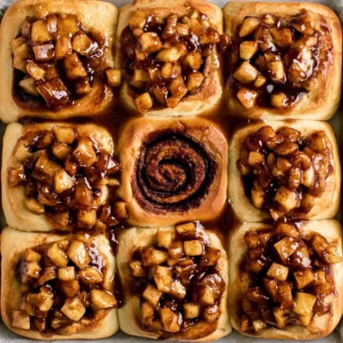 Delicious apple pie cinnamon rolls topped with frosting on a wooden table