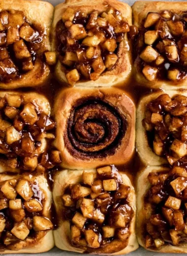 Delicious apple pie cinnamon rolls topped with frosting on a wooden table