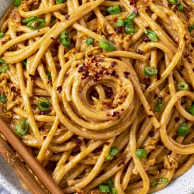 Plate of cozy vegan garlic noodles topped with fresh herbs and chili flakes.