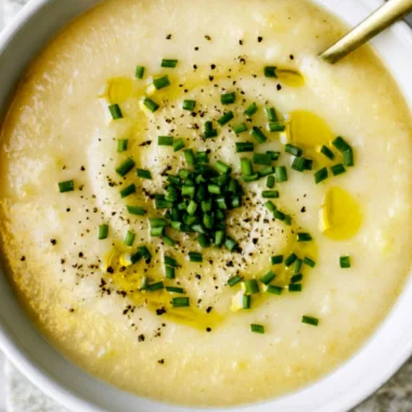 Bowl of creamy potato leek soup garnished with chives and served with bread.