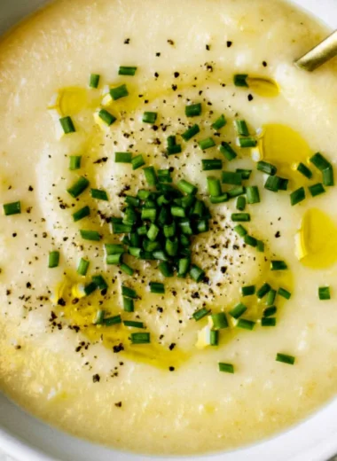 Bowl of creamy potato leek soup garnished with chives and served with bread.