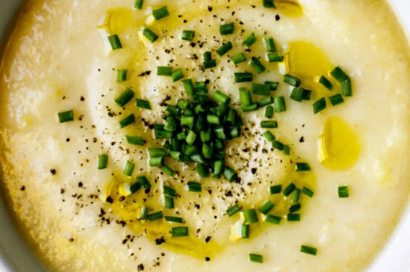 Bowl of creamy potato leek soup garnished with chives and served with bread.