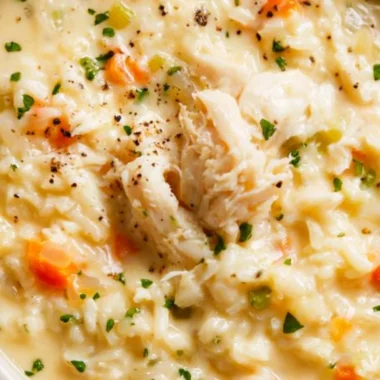 A bowl of creamy chicken rice soup garnished with herbs.